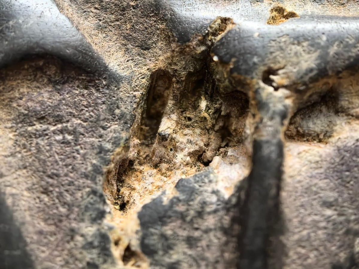 Површината под микроскоп открива метални вградени честички и траги од ерозија